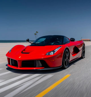 A Ferrari LaFerrari sold at Sandbox Motors driving along a scenic coastal highway in Southern California